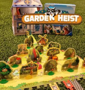 Colorful board game "Garden Heist" displayed on green grass, featuring a detailed game board with various garden elements, playful raccoon characters, and a charming house backdrop. Ideal for family game night and strategy enthusiasts.