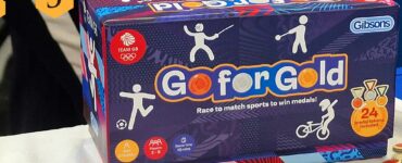 Go for Gold board game by Gibsons displayed at UK Games Expo, featuring colorful box art and sports-themed medal tokens. Suitable for ages 5 and up, designed for 2 to 8 players with a quick game time of 10 minutes.