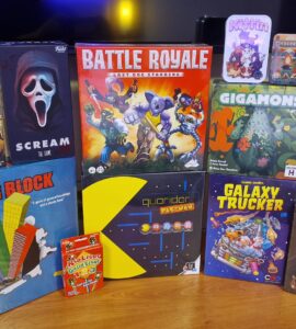 A collection of board games displayed on a wooden surface, featuring titles such as "Forever Home," "Scream: The Game," "Battle Royale," "Gigamons," "Tower Block," "Quoridor Pac-Man," "Galaxy Trucker," and "Paper Dungeons: Side Quest Expansion." The image showcases various game boxes with colorful artwork, appealing to board game enthusiasts.