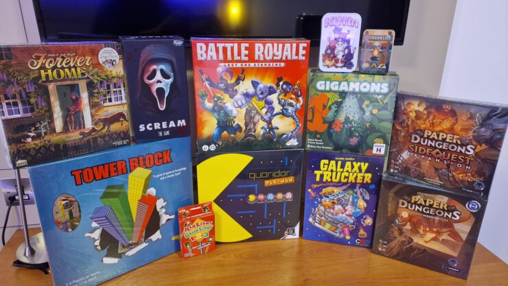 A collection of board games displayed on a wooden surface, featuring titles such as "Forever Home," "Scream: The Game," "Battle Royale," "Gigamons," "Tower Block," "Quoridor Pac-Man," "Galaxy Trucker," and "Paper Dungeons: Side Quest Expansion." The image showcases various game boxes with colorful artwork, appealing to board game enthusiasts.