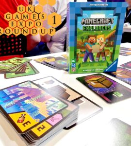 Image of the "Minecraft Explorers" cooperative card game by Ravensburger displayed at the UK Games Expo. The game box is prominently featured alongside various game cards spread out on a table, showcasing colorful graphics and gameplay elements. The background includes blurred figures, hinting at a lively expo atmosphere.