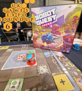 Board game "Robot Quest Arena" showcased at UK Games Expo Roundup 6, featuring colorful game pieces and a detailed game board. The image captures the vibrant box art alongside the gameplay in progress, with attendees visible in the background.