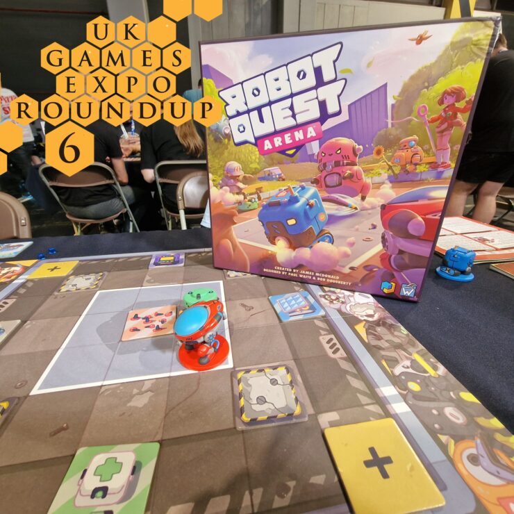 Board game "Robot Quest Arena" showcased at UK Games Expo Roundup 6, featuring colorful game pieces and a detailed game board. The image captures the vibrant box art alongside the gameplay in progress, with attendees visible in the background.