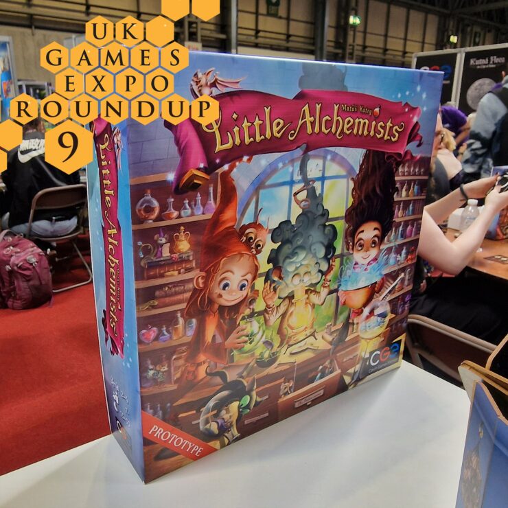 Colorful board game box for "Little Alchemists" displayed at the UK Games Expo, featuring whimsical characters engaged in potion-making. The box is labeled as a prototype and showcases vibrant artwork that captures the theme of alchemy and magic.