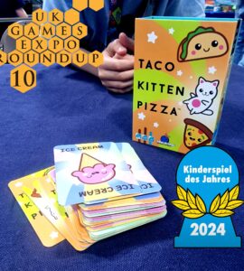 Colorful game box of "Taco Cat Goat Cheese Pizza" displayed at the UK Games Expo 2024, featuring playful illustrations of food characters. Stacked cards include "Ice Cream" design, emphasizing the game's fun and engaging nature. Awarded "Kinderspiel des Jahres 2024," highlighting its popularity among family-friendly games.
