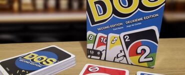 Image of the DOS card game by Mattel, featuring the second edition box and playing cards on a wooden table. The game emphasizes fun for family and friends, with colorful cards showcasing numbers and special symbols. In the foreground, a banner indicates "Summer Marathon 2024."