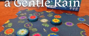 Board game "A Gentle Rain" by Kevin Wilson displayed with game pieces and a promotional card, featuring vibrant floral designs on a puzzle-like game board. The image highlights the game's relaxing theme, suitable for ages 8 and up, and is part of the Summer Marathon 2024 event.