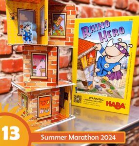 Colorful display of the "Rhino Hero" card game by HABA, featuring a stacked tower of cardboard rooms with playful illustrations, set against a brick background. The image promotes the Summer Marathon 2024 event, showcasing the game's vibrant box and character figures.