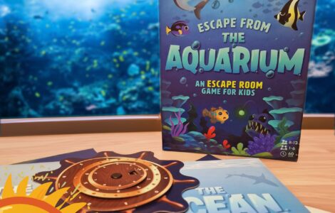 Colorful game box for "Escape from the Aquarium," an escape room game designed for kids aged 8-12, featuring underwater themes and playful graphics, displayed alongside game components on a table with an aquarium backdrop.