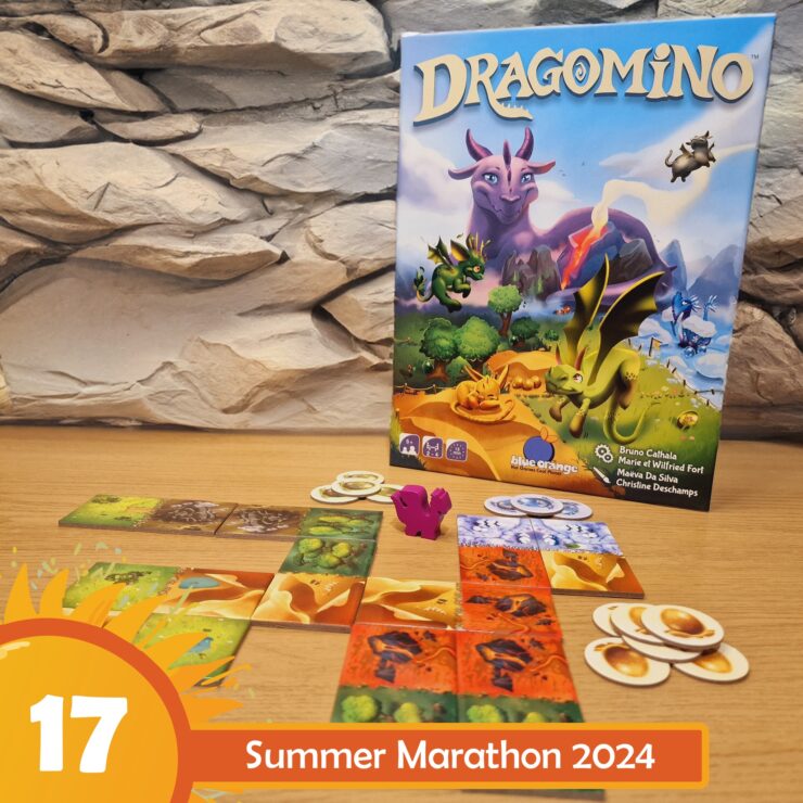 Colorful board game "Dragomino" displayed on a wooden table, featuring vibrant tiles and a pink dragon figure. The game box, illustrated with dragons and a fantasy landscape, is positioned against a textured stone backdrop. The image promotes the Summer Marathon 2024 event.