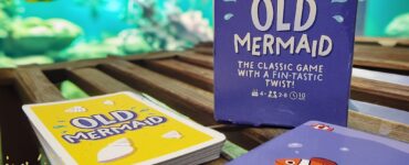 Old Mermaid card game by Professor Puzzle Games displayed on a wooden surface, featuring colorful cards and a vibrant underwater background, promoting Summer Marathon 2024. Suitable for 4+ players, ages 8 and up, with a playful twist on a classic game.