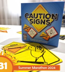 Caution Signs party game box displayed on a table with colorful sketch cards featuring humorous prompts. The image highlights the game's fun and interactive nature, suitable for gatherings and creative play. Summer Marathon 2024 branding is visible in the corner.