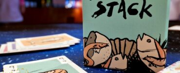 Sakana Stack card game box displayed on a table with playing cards featuring shrimp illustrations, set against a colorful background; Summer Marathon 2024 event highlighted in the corner.