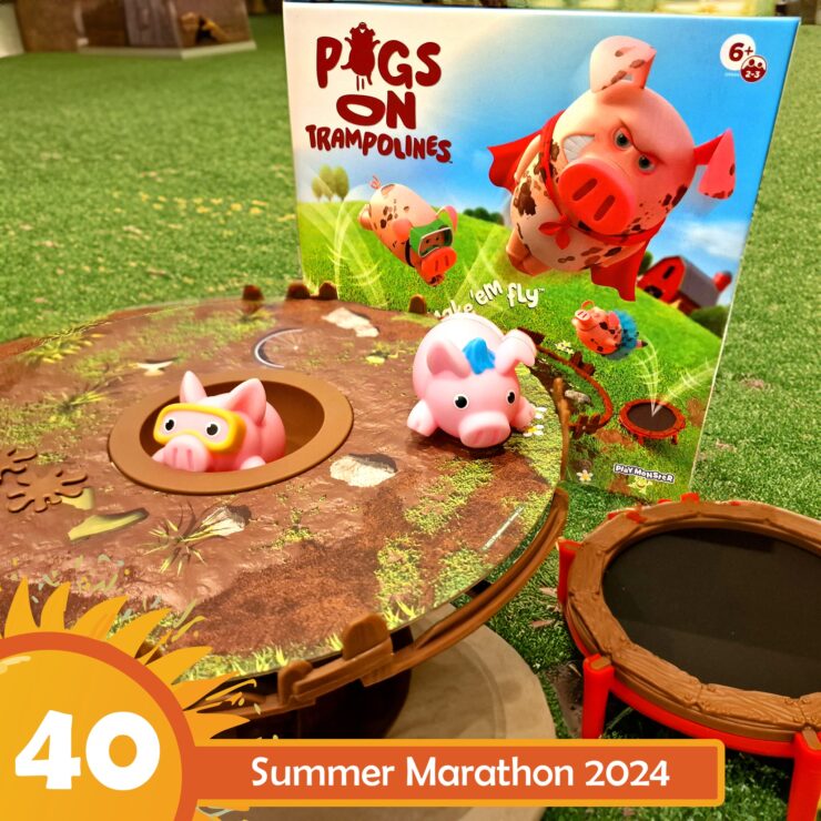 Colorful game setup of "Pigs on Trampolines," featuring two pig figures on a trampoline-like base, with the game box in the background. Ideal for children ages 6 and up, promoting fun and interactive play. Summer Marathon 2024 event branding visible in the corner.