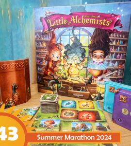 Colorful board game "Little Alchemists" displayed on a wooden table, featuring vibrant artwork of characters engaging in potion-making. The game box, cards, and tokens are arranged alongside a themed background, promoting the Summer Marathon 2024 event.
