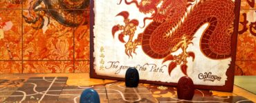 Alt text: Tsuro board game displayed with vibrant dragon artwork, featuring game pieces in blue and red on a winding path. Background includes intricate patterns and the title "Summer Marathon 2024" in the corner, emphasizing a gaming event theme.