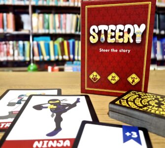 Board game "Steery" displayed with character cards, including a ninja, on a wooden table in front of a library backdrop. The game is suitable for 3-8 players, takes approximately 30 minutes to play, and is recommended for ages 10 and up.