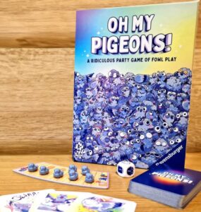 Board game "Oh My Pigeons!" by Ravensburger featuring colorful artwork, game cards, dice, and player pieces, set against a wooden background. Ideal for family game nights and parties.