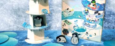 Colorful display of the board game "High Rise Penguins," featuring a multi-level penguin tower, game box, and decorative blue gems on a blue background. Ideal for family game nights and penguin enthusiasts.