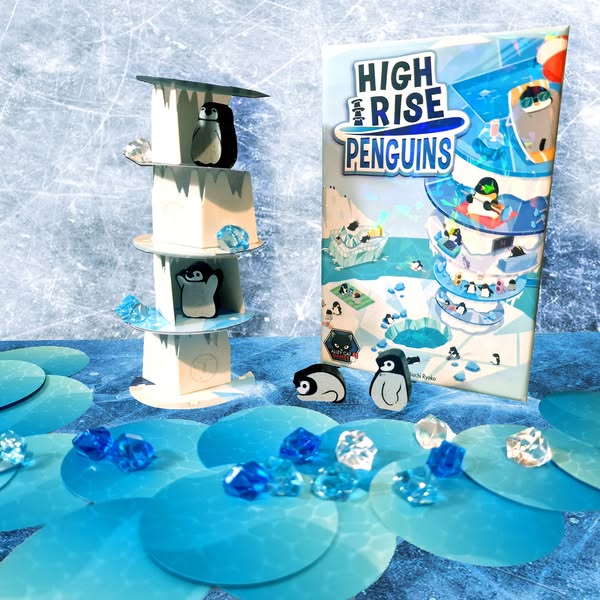 Colorful display of the board game "High Rise Penguins," featuring a multi-level penguin tower, game box, and decorative blue gems on a blue background. Ideal for family game nights and penguin enthusiasts.