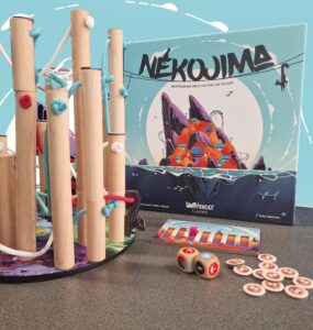 Nekojima board game setup featuring colorful wooden poles, ropes, and game components on a table, with the game box displaying vibrant artwork. Ideal for family fun and strategy play.