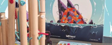 Nekojima board game setup featuring colorful wooden poles, ropes, and game components on a table, with the game box displaying vibrant artwork. Ideal for family fun and strategy play.