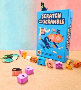 Colorful board game "Scratch and Scramble" displayed with its box and various playful tokens and pieces on a textured surface. The game features whimsical illustrations of animals and objects, making it visually appealing for family game nights.