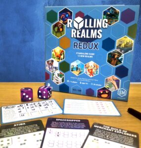 Board game "Rolling Realms: Redux" displayed with game components including dice and player sheets. The game is designed for 1-6 players, ages 14 and up, and features 12 new realms with a playtime of approximately 30 minutes.