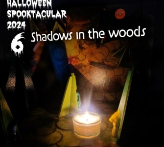 Halloween Spooktacular 2024 promotional image featuring the title "Shadows in the Woods." The scene includes colorful wooden figures and a lit candle, creating an eerie ambiance suitable for Halloween festivities.
