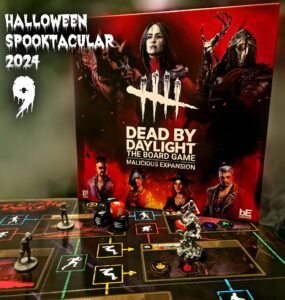 Dead by Daylight: The Board Game - Malicious Expansion displayed for Halloween Spooktacular 2024, featuring game box art and miniatures on the game board with action elements, dice, and character tokens.