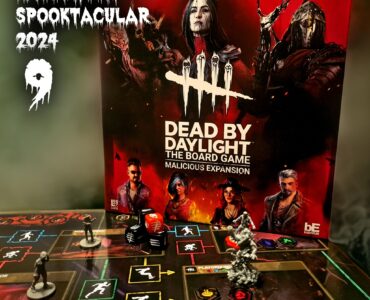 Dead by Daylight: The Board Game - Malicious Expansion displayed for Halloween Spooktacular 2024, featuring game box art and miniatures on the game board with action elements, dice, and character tokens.