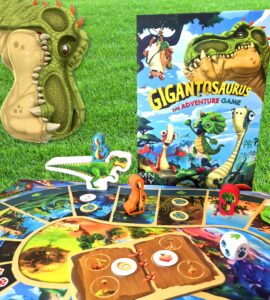 Colorful Gigantosaurus board game setup featuring a dinosaur-themed game board, character pieces, and the game box, all displayed on green grass. Perfect for family game nights and children's entertainment.