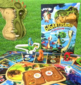 Colorful Gigantosaurus board game setup featuring a dinosaur-themed game board, character pieces, and the game box, all displayed on green grass. Perfect for family game nights and children's entertainment.