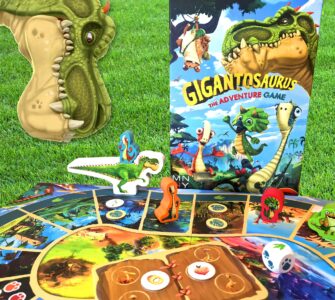 Colorful Gigantosaurus board game setup featuring a dinosaur-themed game board, character pieces, and the game box, all displayed on green grass. Perfect for family game nights and children's entertainment.
