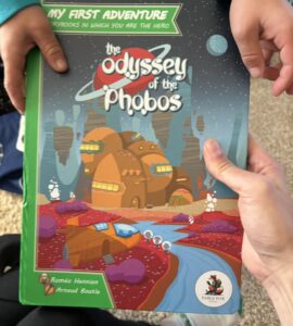 Child holding "The Odyssey of the Phobos" book from the "My First Adventure" series, featuring vibrant space-themed illustrations and engaging storyline. Ideal for young readers seeking interactive storytelling experiences.