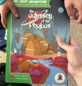 Child holding "The Odyssey of the Phobos" book from the "My First Adventure" series, featuring vibrant space-themed illustrations and engaging storyline. Ideal for young readers seeking interactive storytelling experiences.