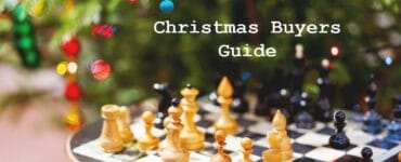Chessboard with wooden pieces in front of a decorated Christmas tree, featuring a text overlay that reads "Christmas Buyers Guide." Ideal for holiday gift ideas related to chess and games.