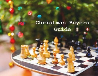 Chessboard with wooden pieces in front of a decorated Christmas tree, featuring a text overlay that reads "Christmas Buyers Guide." Ideal for holiday gift ideas related to chess and games.