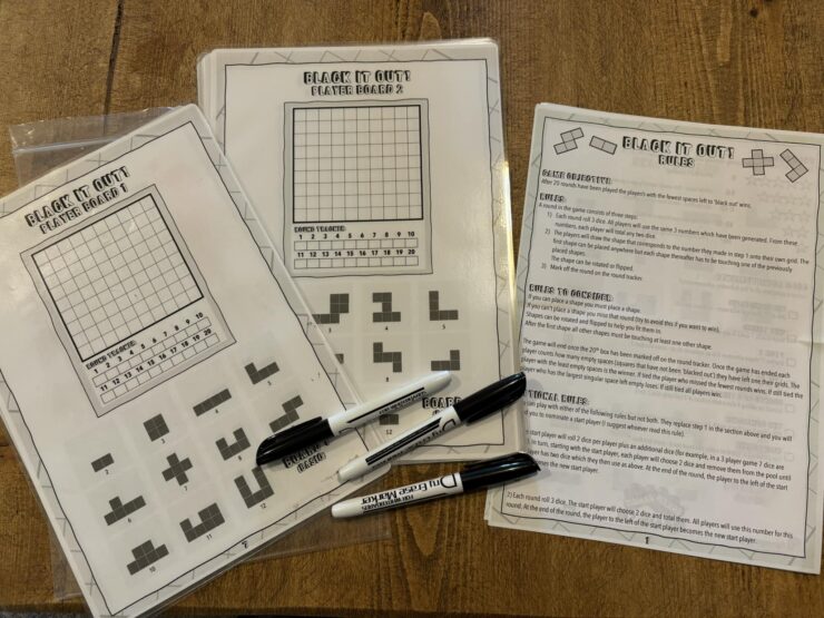 Printable game sheets for "Black It Out!" featuring player boards and game rules. The image showcases two player boards with grids and shapes, along with a rules sheet explaining gameplay and objectives. Markers are placed beside the sheets, ready for use.