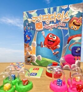 Colorful board game "Jumping Dice" featuring cartoon dice characters, game components including dice, cards, and a bell, set against a blue sky background.
