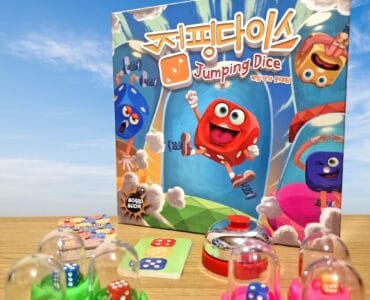 Colorful board game "Jumping Dice" featuring cartoon dice characters, game components including dice, cards, and a bell, set against a blue sky background.