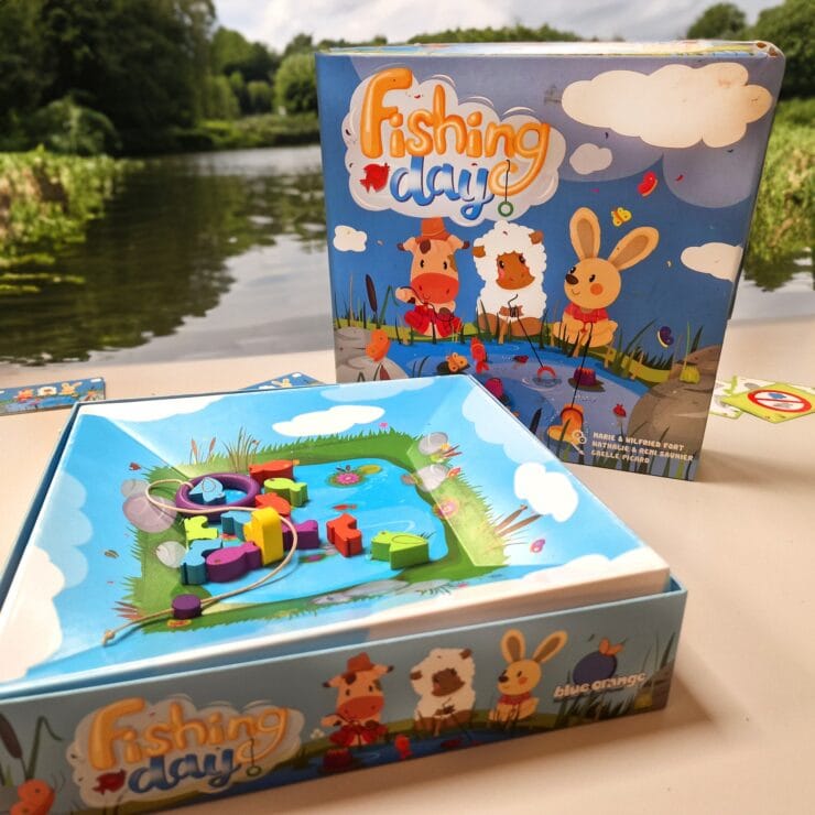 Colorful board game "Fishing Day" featuring a playful fishing scene, with vibrant wooden pieces and a scenic backdrop of a river and greenery. Ideal for family fun and skill development.