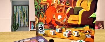 Image of the board game "My Shelfie: The Dice Game" featuring a playful cat on the box cover, alongside game components including dice and a score sheet. The background shows a modern living space with bookshelves and decor, creating a cozy atmosphere for family game night.