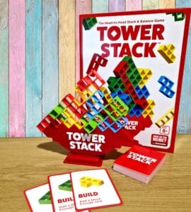 Colorful Tower Stack game set displayed on a wooden table, featuring a vibrant stacking tower, game cards, and the game box in the background. Ideal for family fun and skill development, suitable for ages 8 and up.