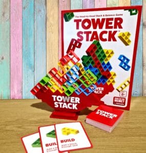 Colorful Tower Stack game set displayed on a wooden table, featuring a vibrant stacking tower, game cards, and the game box in the background. Ideal for family fun and skill development, suitable for ages 8 and up.