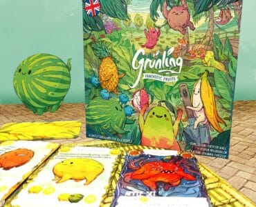 Colorful board game "Grünling: Fantastic Fruits" featuring whimsical fruit characters, surrounded by game cards and a playful watermelon illustration. Ideal for family game nights and children’s entertainment.