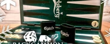 Backgammon game set featuring a green Carlsberg-themed board, dice, and game pieces, with decorative snowflakes in the background. Perfect for holiday gatherings and game nights.