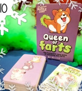 Colorful image of the "Queen of Farts" card game by Professor Puzzle Games, featuring a playful corgi on the box and illustrated animal characters on the cards. The game promotes fun and laughter for ages 8 and up, designed for 2 to 6 players. Background includes green smoke effects, enhancing the playful theme.