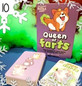 Colorful image of the "Queen of Farts" card game by Professor Puzzle Games, featuring a playful corgi on the box and illustrated animal characters on the cards. The game promotes fun and laughter for ages 8 and up, designed for 2 to 6 players. Background includes green smoke effects, enhancing the playful theme.