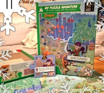 Colorful jigsaw puzzle box titled "My Puzzle Adventure: Dragon," featuring an illustrated map with a castle, characters, and interactive puzzle pieces. The image showcases the puzzle's storytelling aspect, with text prompts and a whimsical design suitable for children. Snowflakes are subtly placed around the image, adding a festive touch.